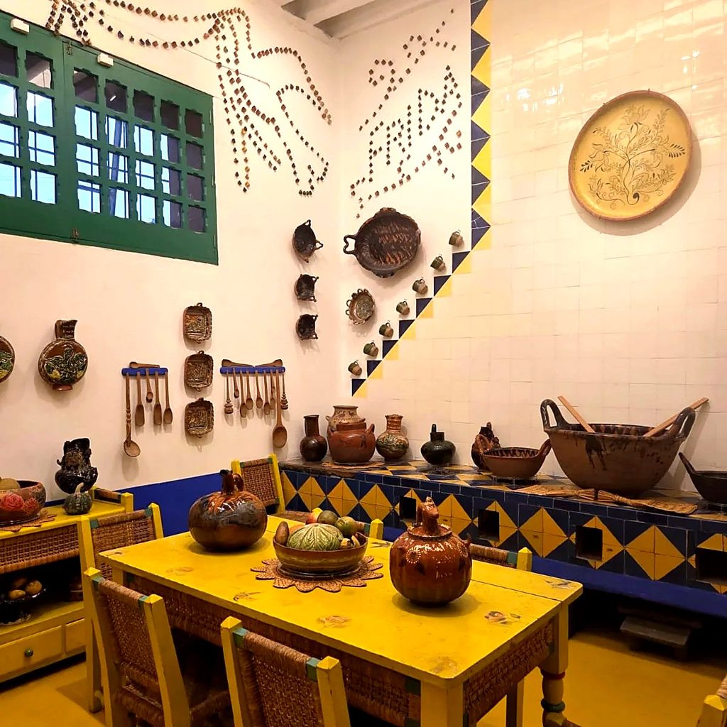 La cuisine de la Casa Azul, avec sa table jaune, ses faïences bleues et jaunes et le prénom Frida en mosaïque sur le mur