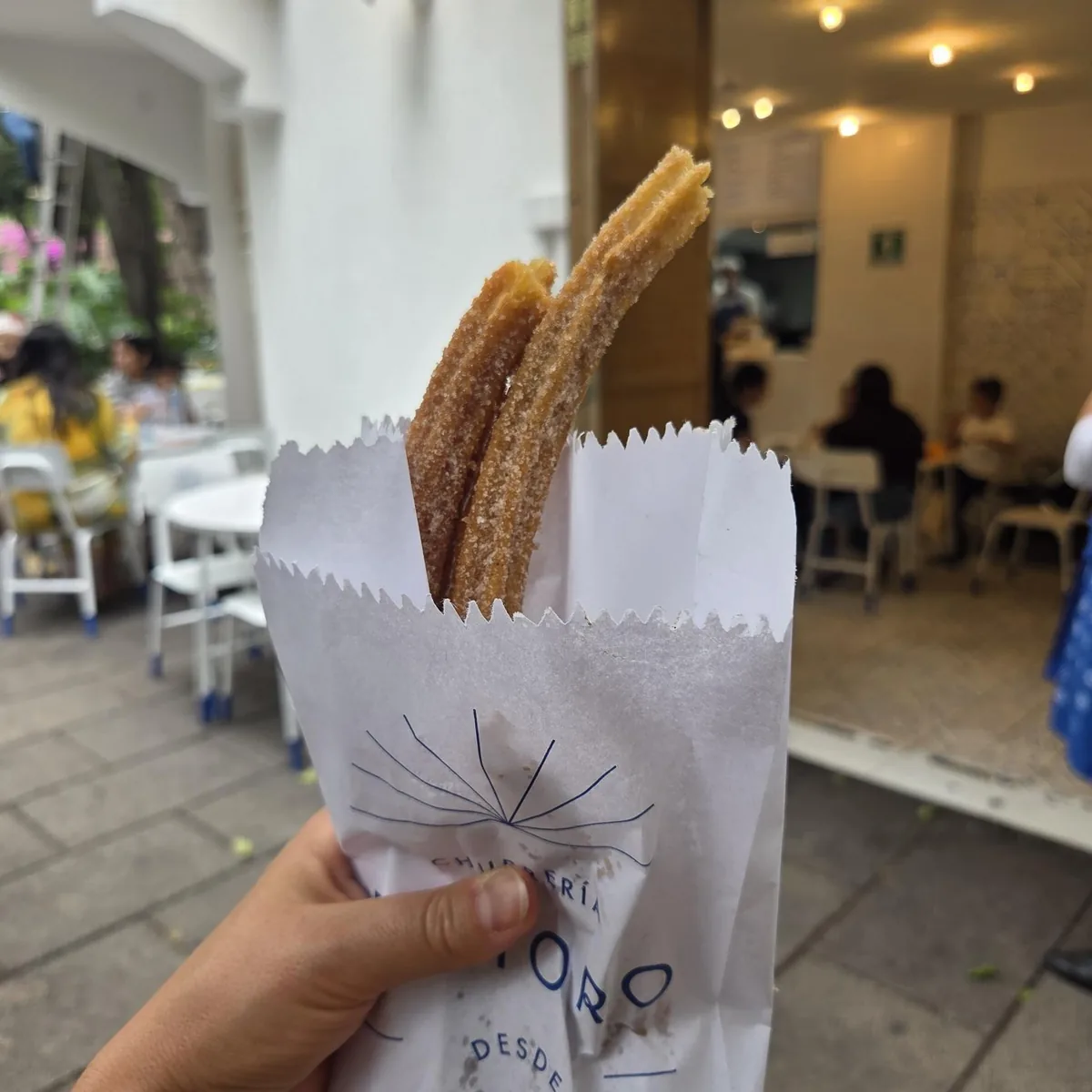 Churros au sucre tenus dans leur sachet en papier, devant la churrería El Moro à Mexico.