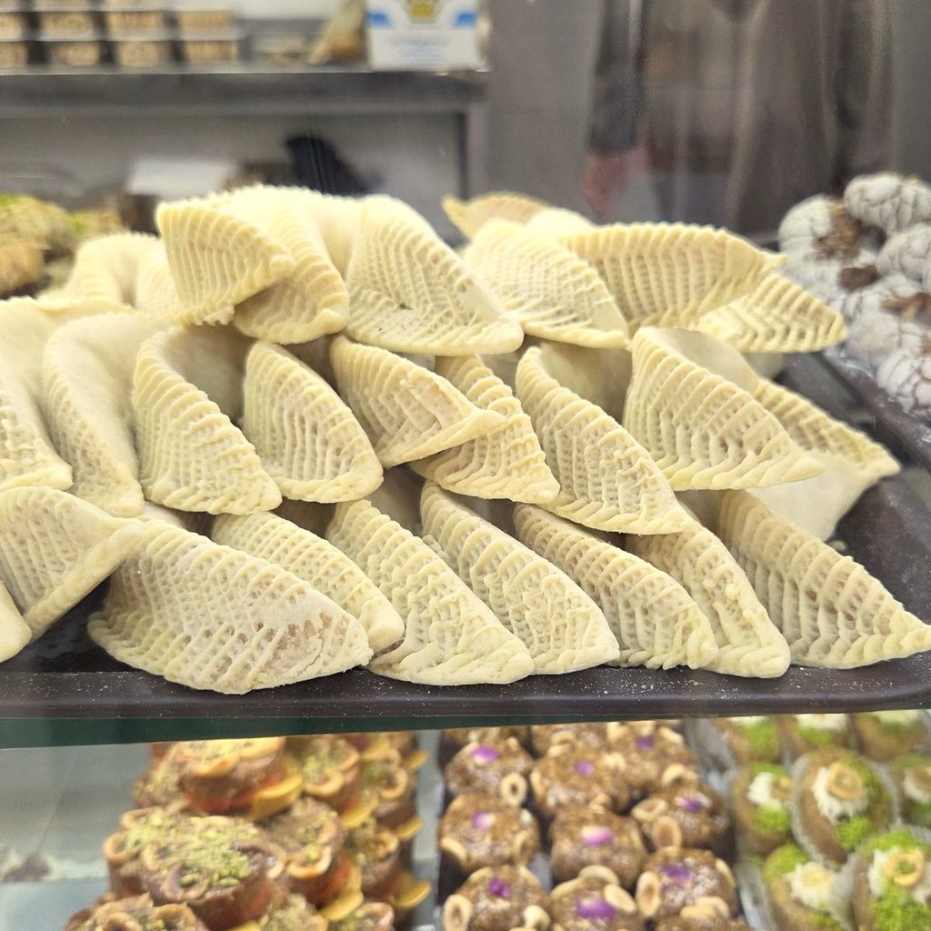 Plateau de cornes de gazelle dans la vitrine d’une pâtisserie marocaine, entouré de ghriba et de gâteaux aux fruits sec