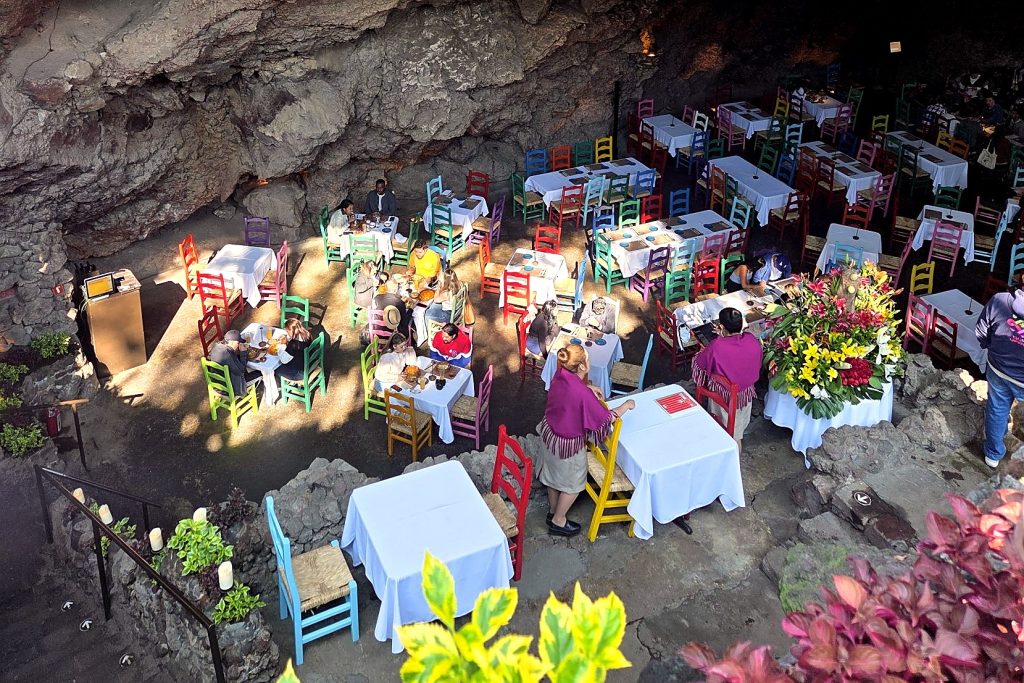 Salle du restaurant La Gruta, près de Teotihuacán, installée dans une grotte : tables aux nappes blanches et chaises colorées, vues d’en haut