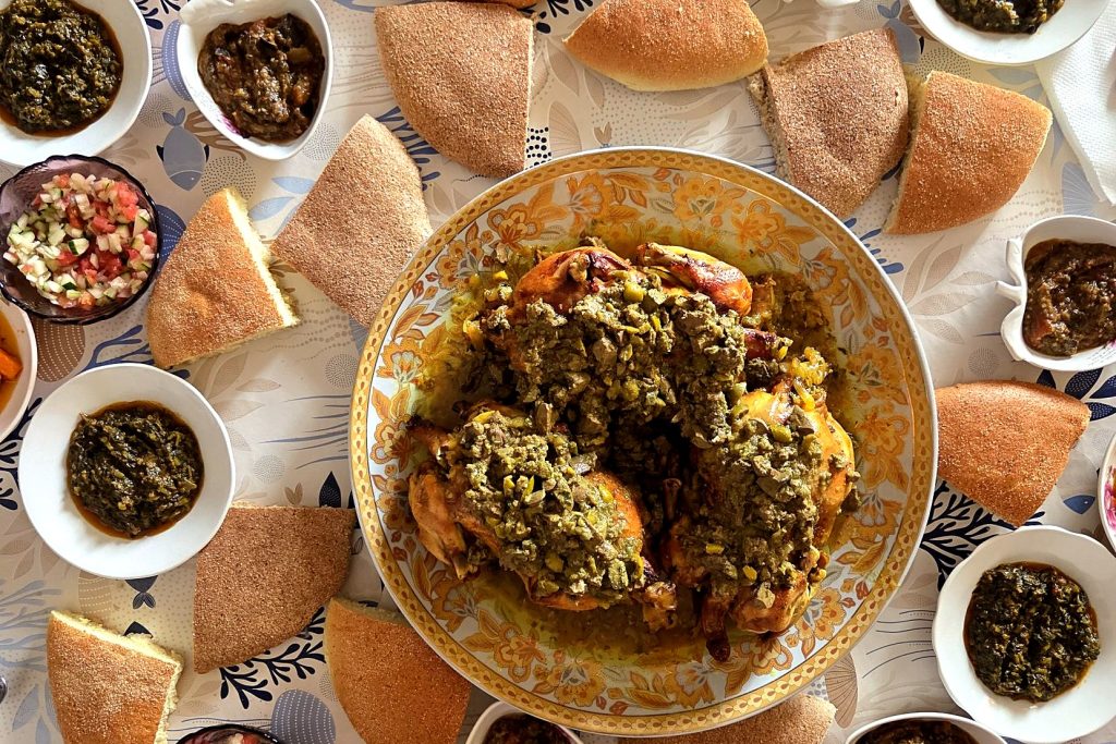 Grand plat de poulet aux olives au centre d’une table familiale marocaine, entouré de pain et de petites salades