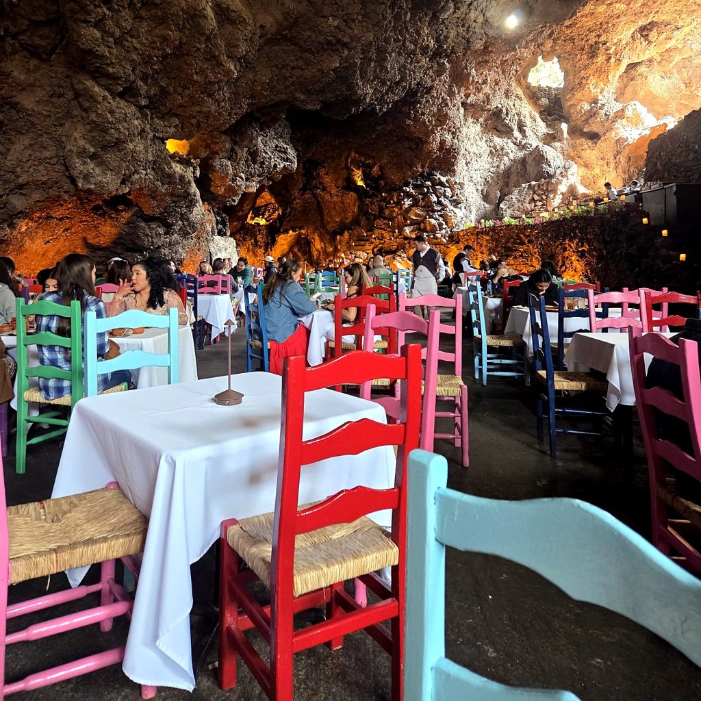 Tables nappées de blanc et chaises en bois peint de toutes les couleurs dans la grotte du restaurant La Gruta, près de Teotihuacán