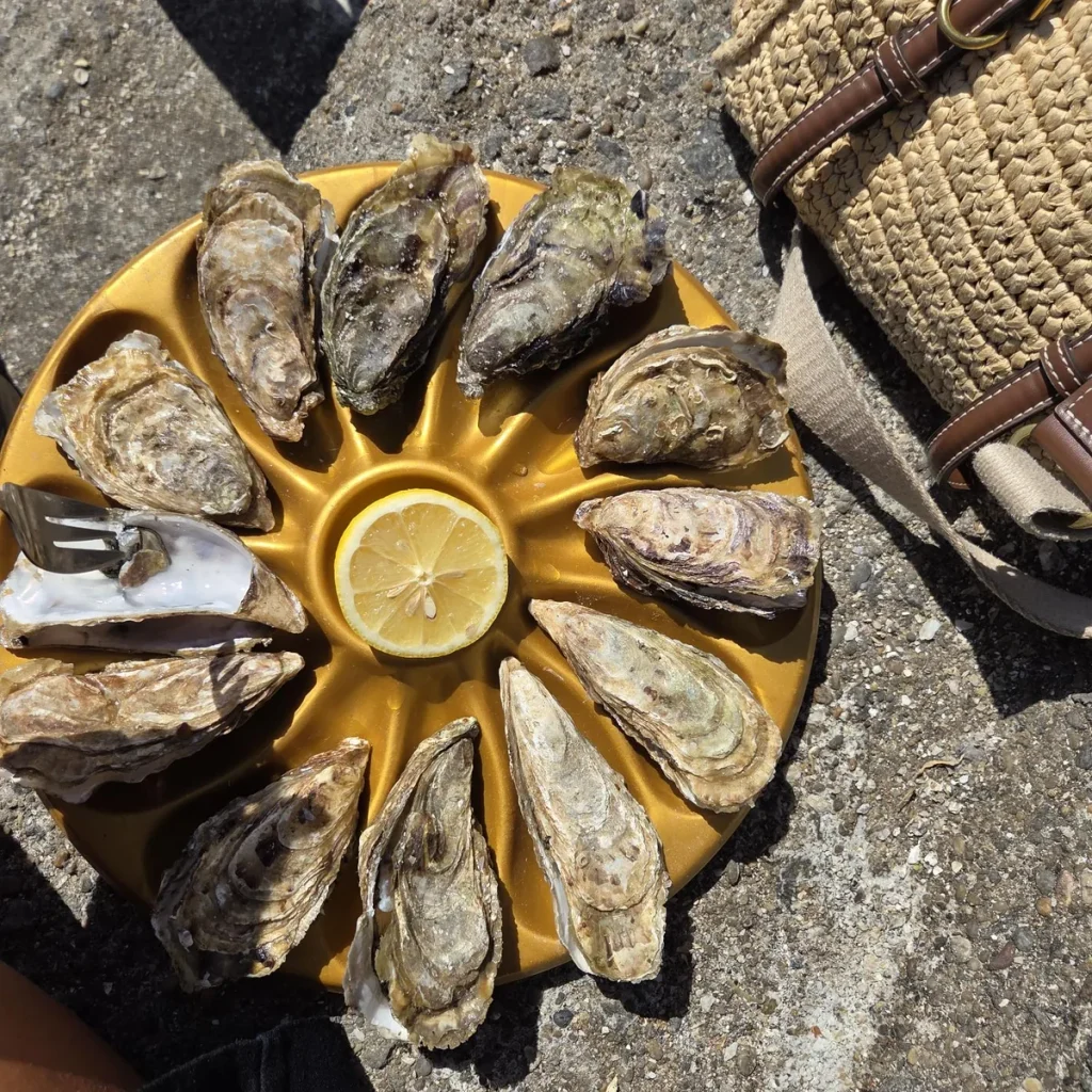 Douzaine d’huîtres disposées en cercle autour d’un demi-citron sur un plateau doré, à côté d’un panier en paille à Cancale, en Bretagne, France.