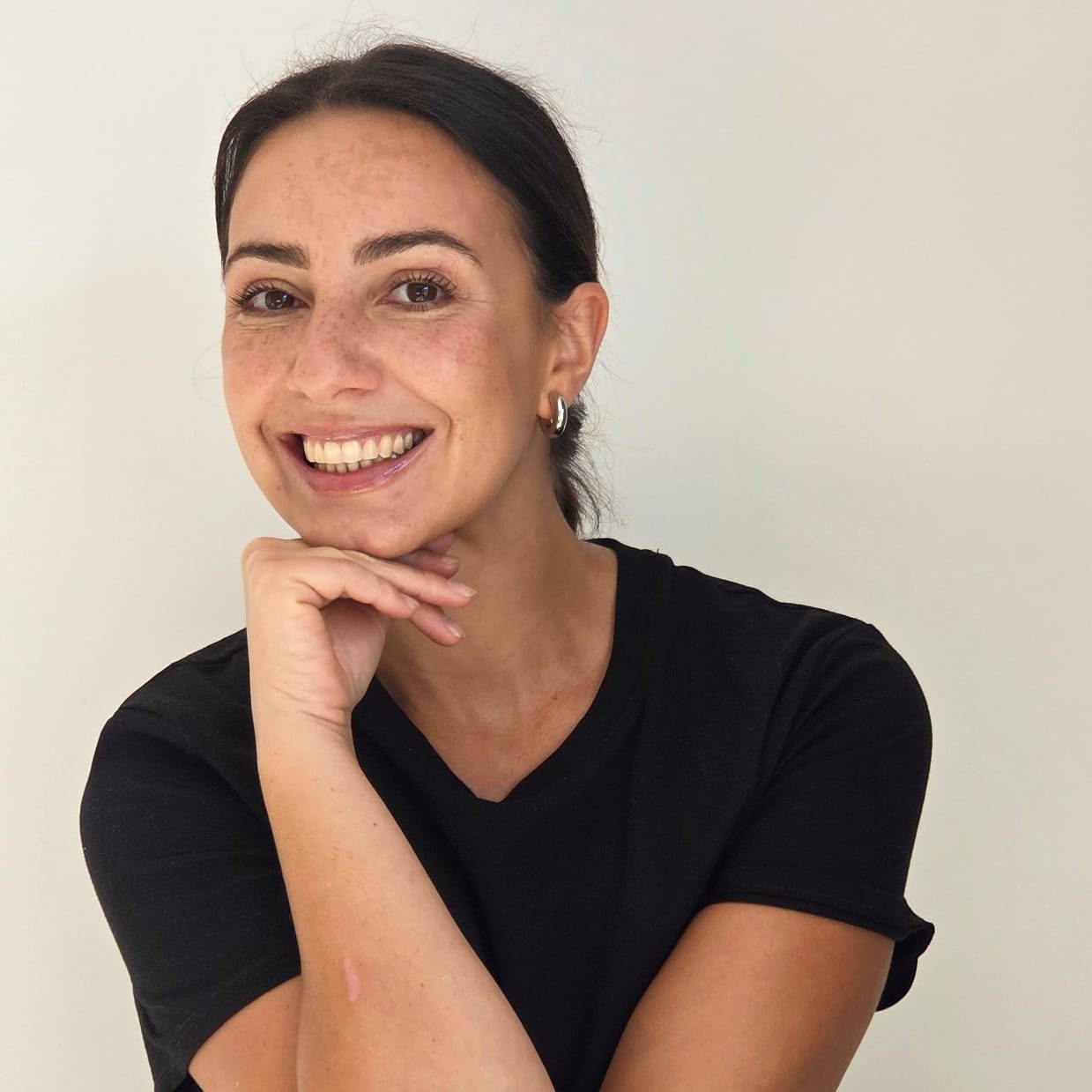 Portrait de Mathilde Lakhdar, cheffe privée à Rennes, souriante, le menton posé sur la main, en t-shirt noir sur fond clair