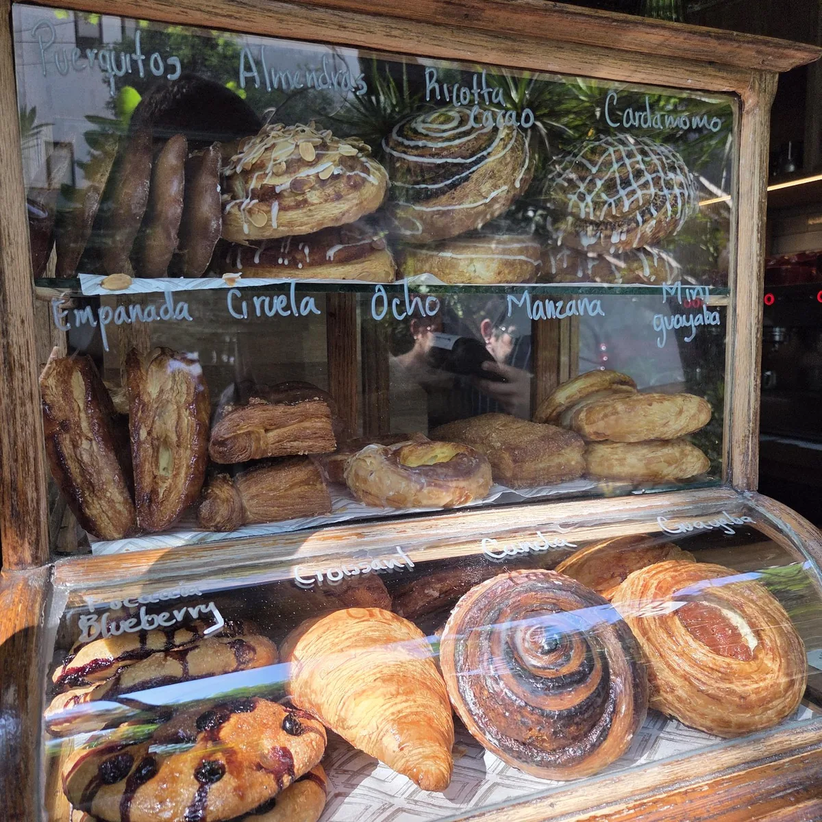 Vitrine en bois de la boulangerie Lardo à Mexico City, remplie de viennoiseries : croissant, roulés à la cannelle, focaccia aux myrtilles.